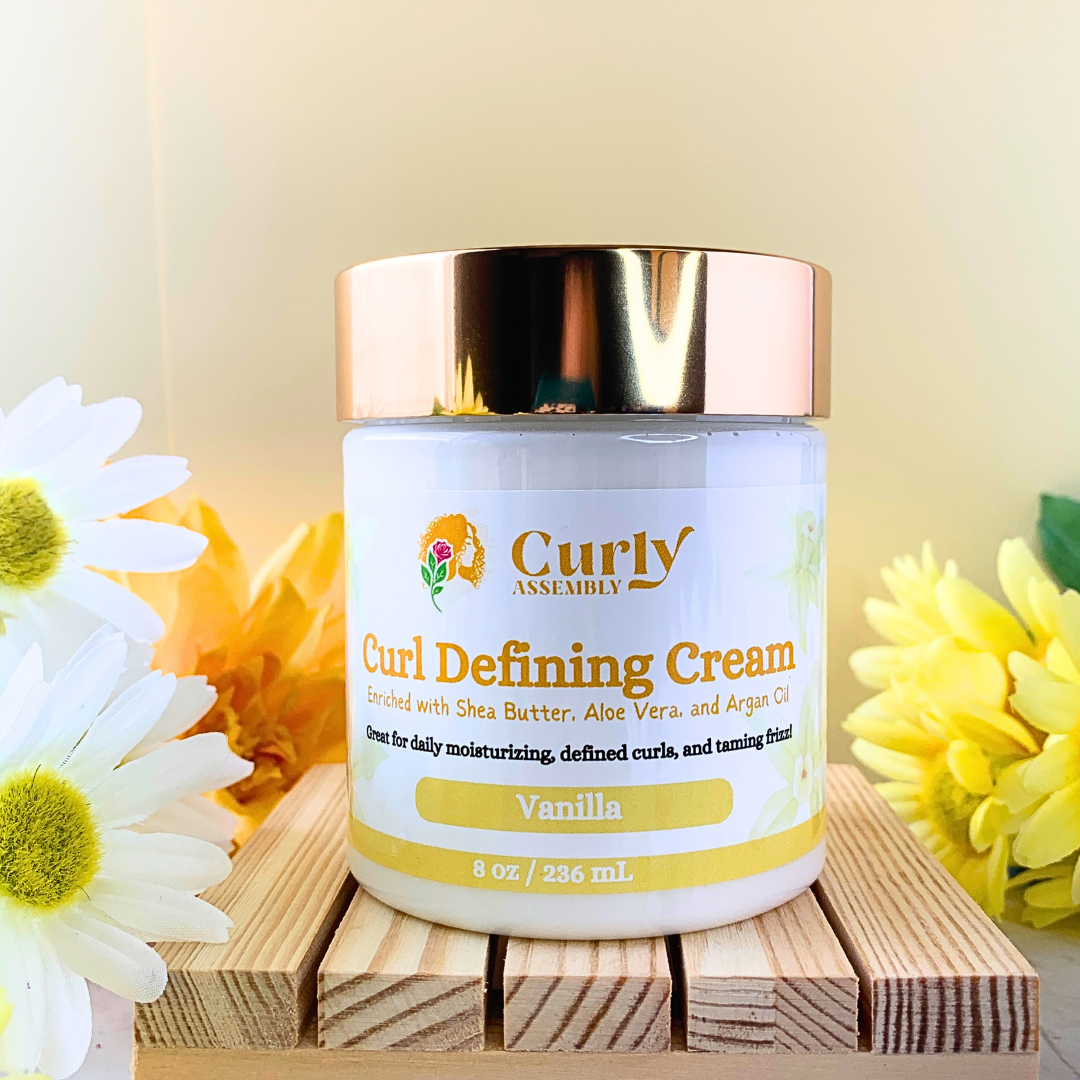 Front-facing jar of Curly Assembly Sweet Vanilla Curl Defining Cream posed with a floral background, highlighting the product's focus on nourishing and defining curls

