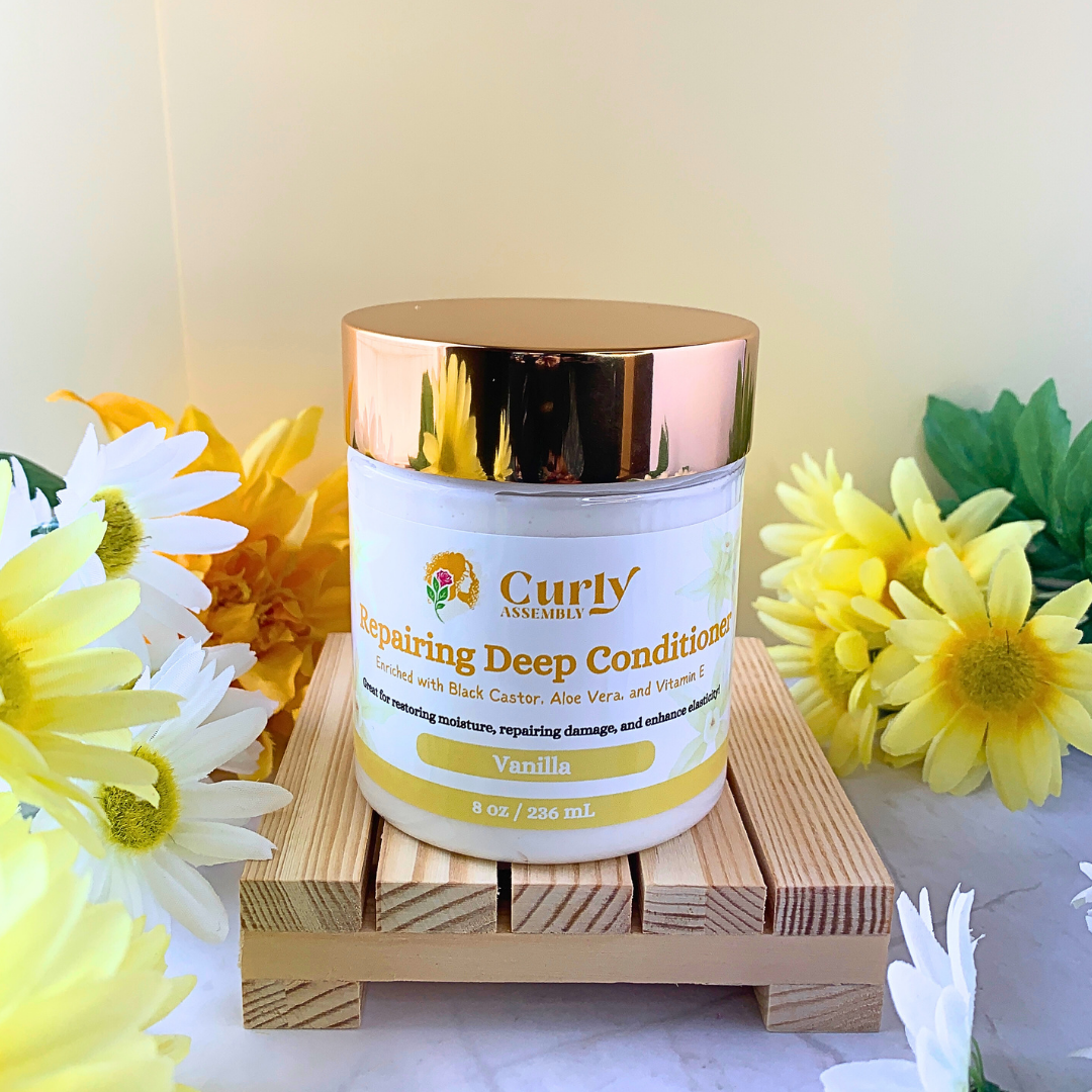 Front-facing jar of Curly Assembly Sweet Vanilla Repairing Deep Conditioner posed with a floral background, featuring a deeply nourishing formula with aloe vera, black castor oil, and sweet almond oil to repair and restore curly hair while providing a soft vanilla scent.